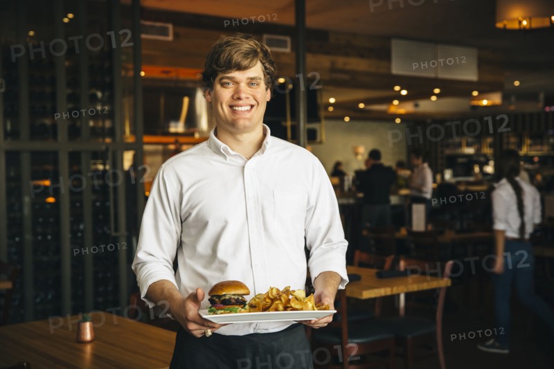 Caucasian waiter carrying cheeseburger and chips in cafe