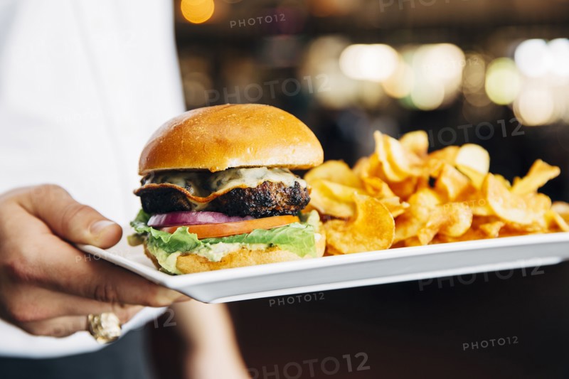 Caucasian waiter carrying cheeseburger and chips in cafe