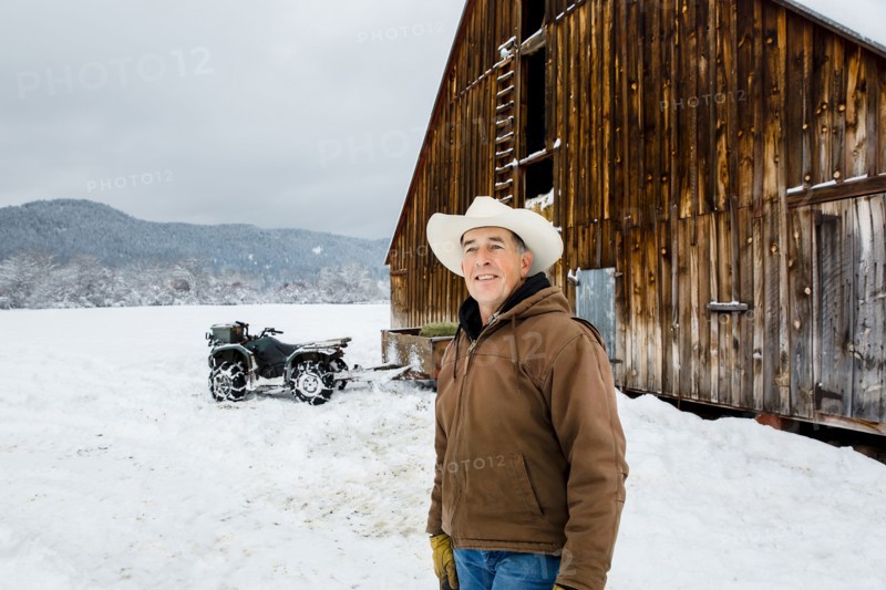 Caucasian farmer smiling near snowy barn
