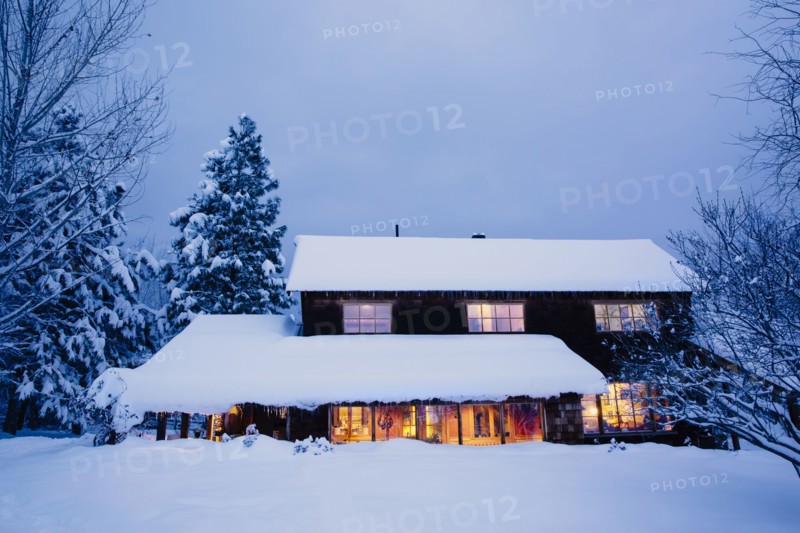 Illuminated house in snowy field at dusk