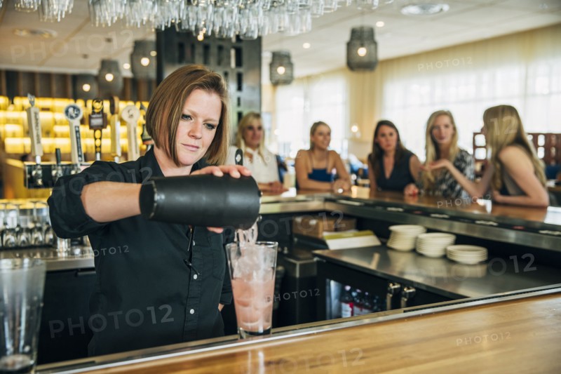 Caucasian bartender pouring cocktail from mixer into glass