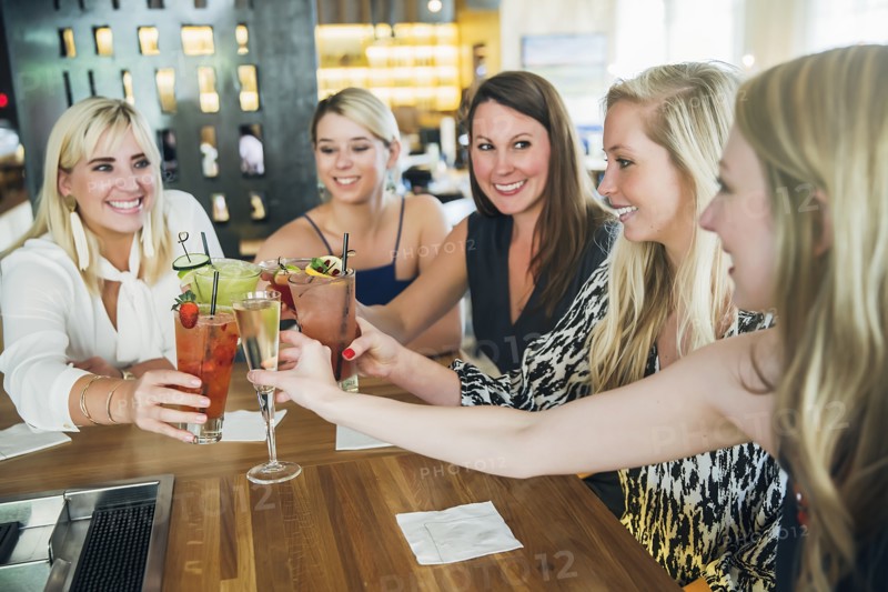 Caucasian women toasting at bar with cocktails