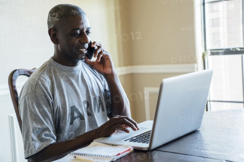 Black man using laptop and cell phone at table