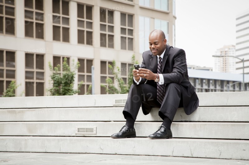 Black businessman sitting on staircase texting on cell phone outdoors