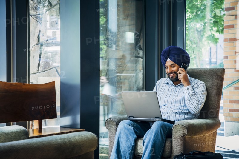 Man wearing turban using laptop and cell phone in armchair