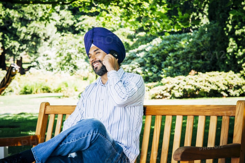 Man wearing turban sitting on park bench talking on cell phone