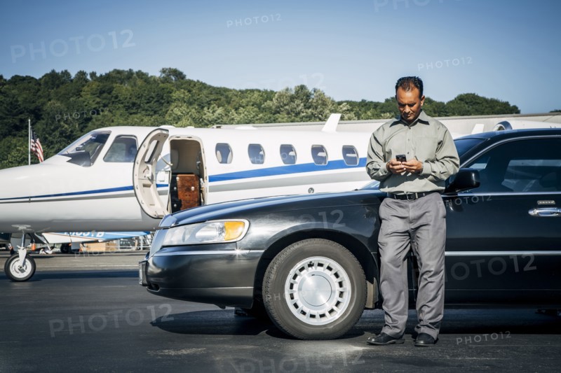 Indian man texting on cell phone at car near airplane
