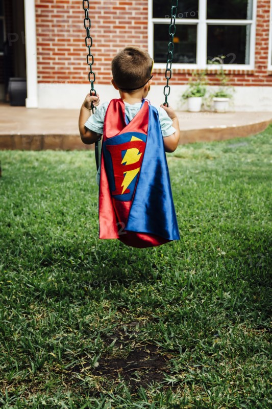 Caucasian boy wearing superhero costume on swing