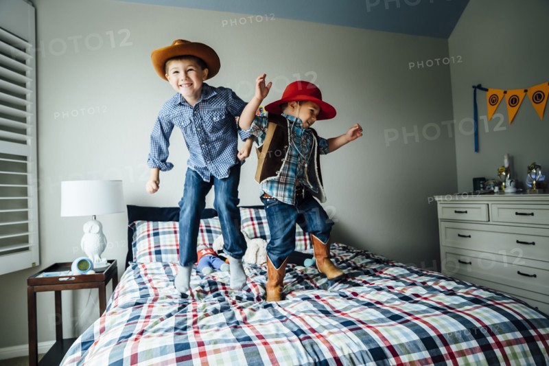 Caucasian boys wearing cowboy costumes jumping on bed