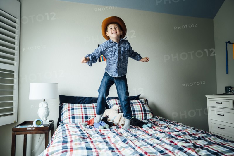 Caucasian boy wearing cowboy costume jumping on bed