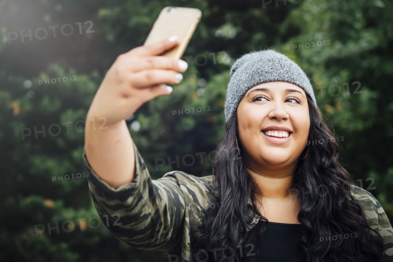Mixed Race woman posing for cell phone selfie in forest
