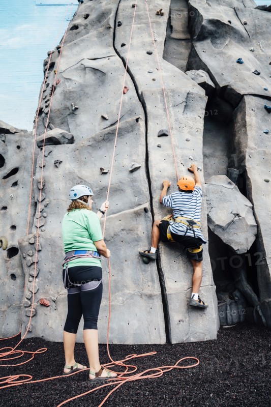 Woman holding rope for man climbing rock climbing wall