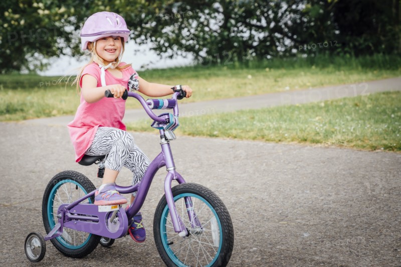 Mixed Race girl riding bicycle with training wheels