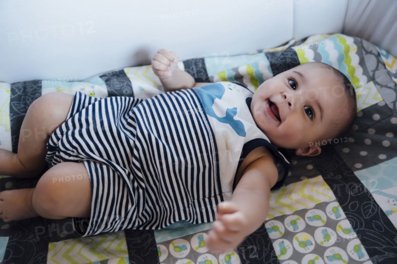 Smiling Mixed Race baby boy laying in crib