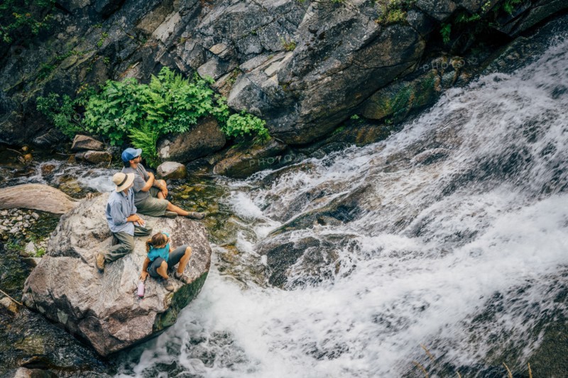 Caucasian people sitting on rock watching river rapids