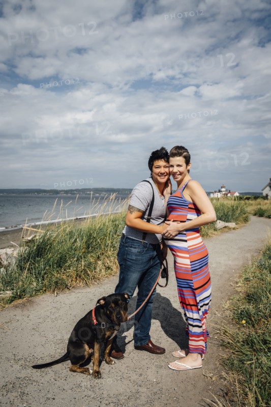 Portrait of pregnant lesbian couple with dog hugging at waterfront