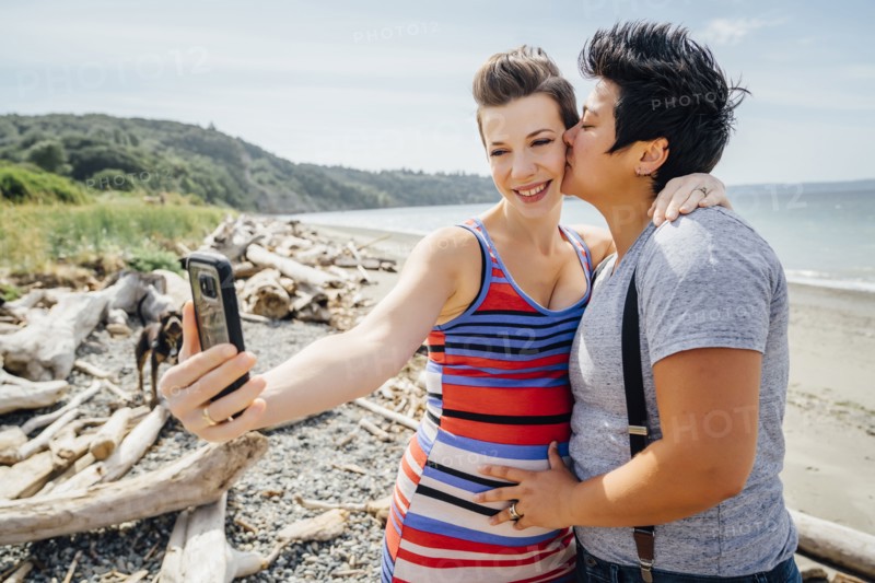 Pregnant lesbian couple posing for cell phone selfie on beach