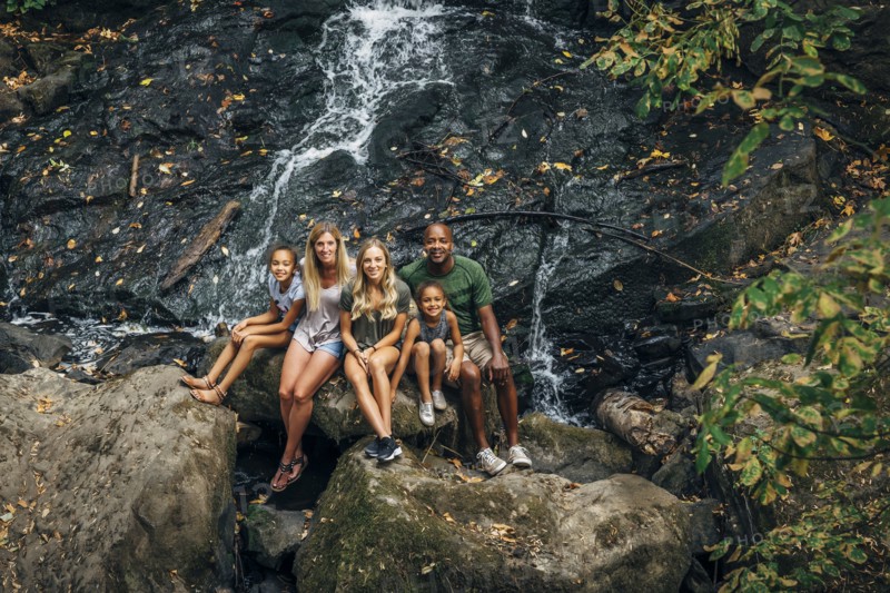 Multi-ethnic family posing on rock near waterfall