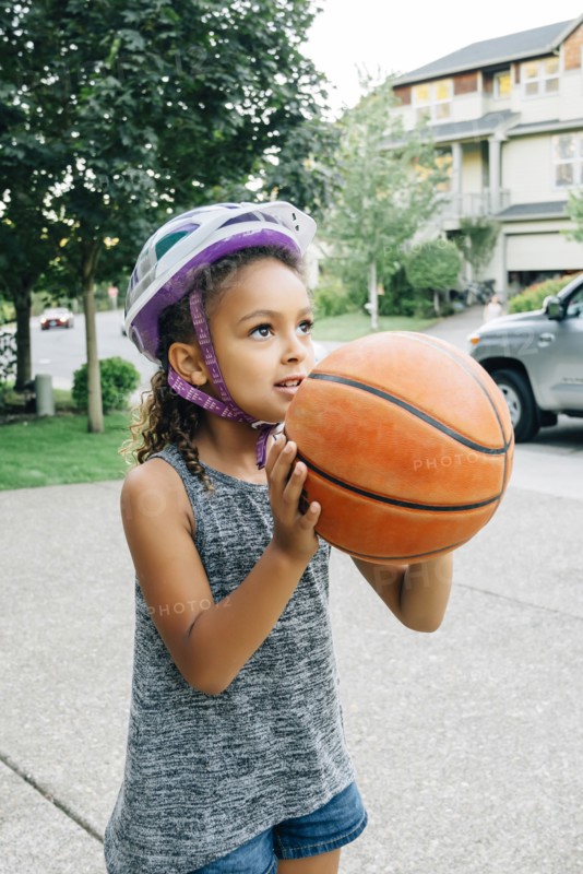 Mixed Race girl wearing helmet playing basketball in driveway