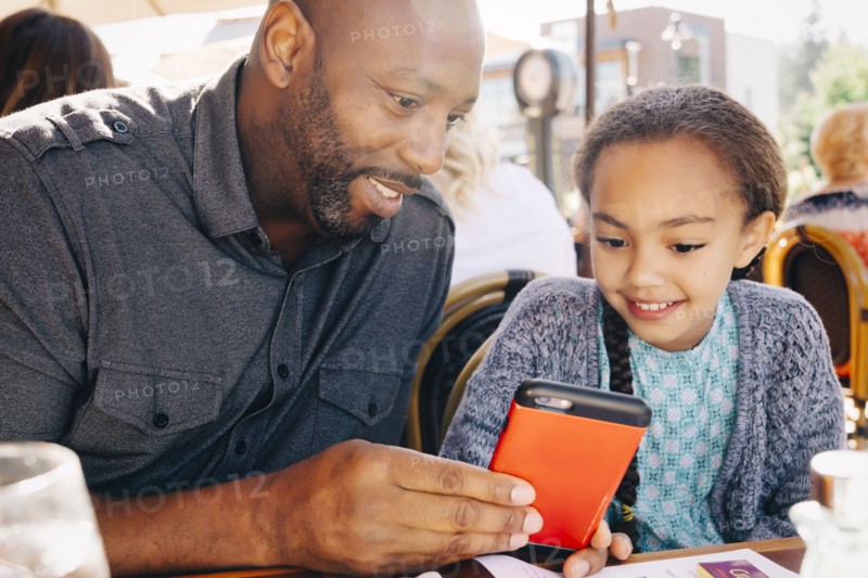 Father and daughter sitting at restaurant table texting on cell phone