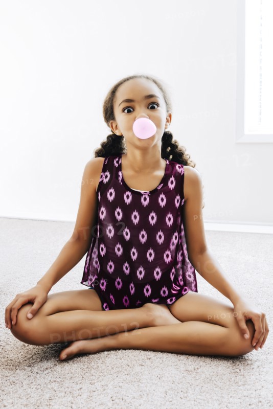 Mixed Race girl sitting on floor blowing bubble with gum