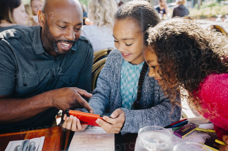 Father ad daughters texting on cell phone at restaurant