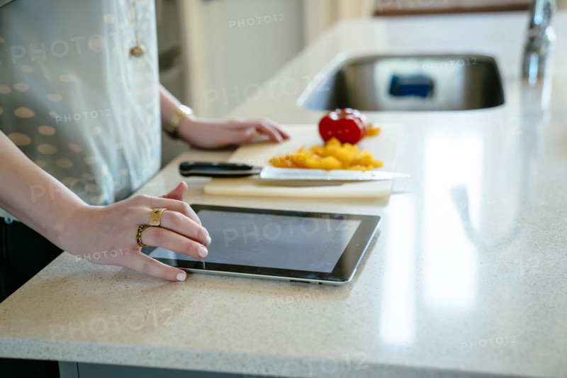 Woman using digital tablet and chopping food in domestic kitchen