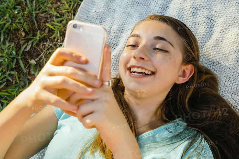 Laughing Caucasian girl laying on blanket texting on cell phone