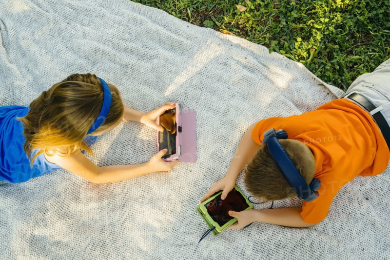 Caucasian brother and sister laying on blanket using technology