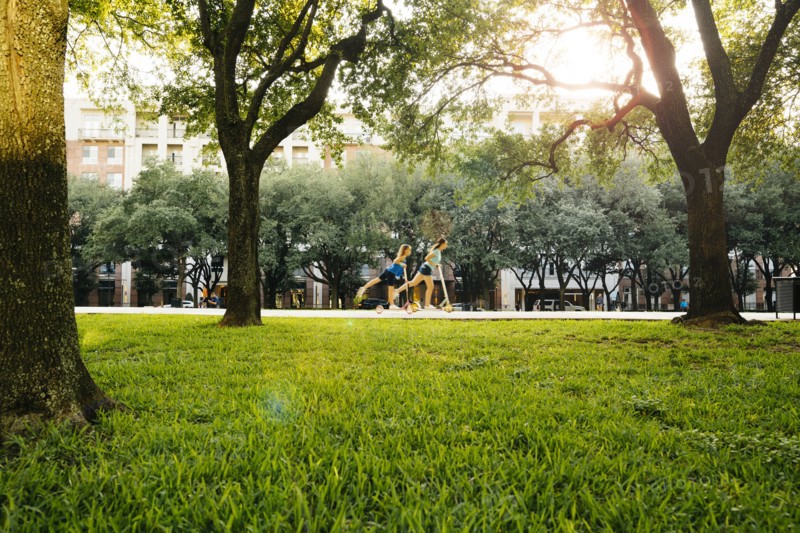 Distant Caucasian girls riding scooter in park