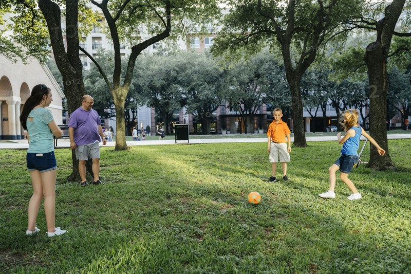 Caucasian family kicking soccer ball in park