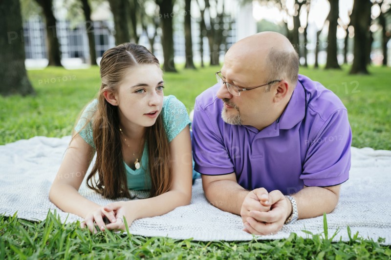 Serious Caucasian father and daughter talking on blanket in park