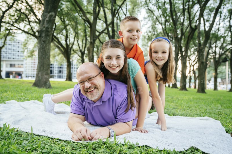 Portrait of Caucasian boy and girls laying on back of father in park