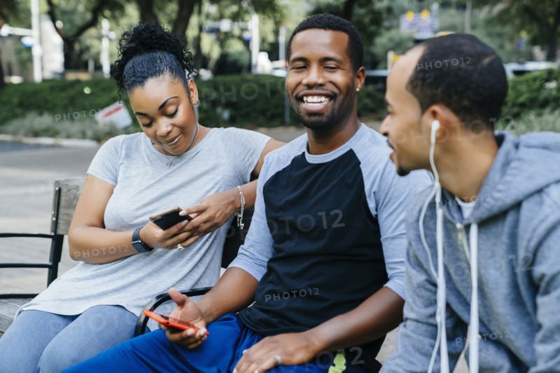 Black friends sitting on bench holding cell phones
