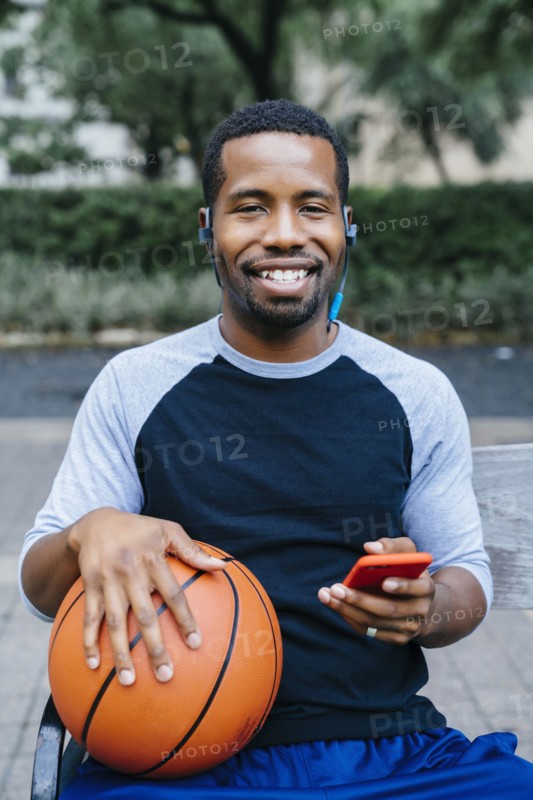 Portrait of Black man listening to earbuds and holding basketball