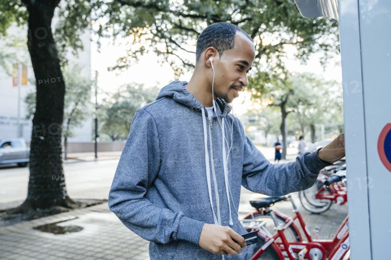 Black man with earbuds paying for bicycle rental with credit card