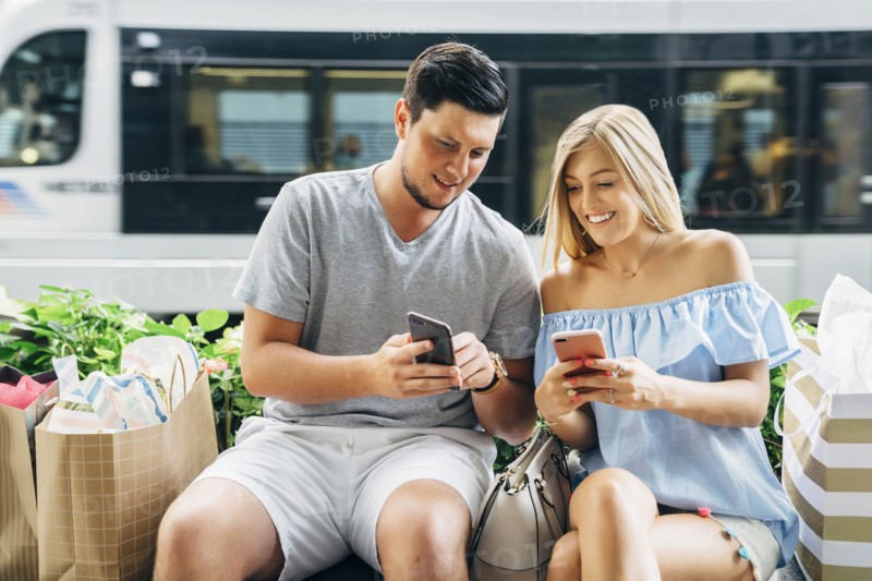 Caucasian couple with shopping bags texting on cell phones near train