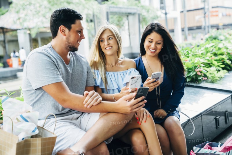 Friends sitting on bench texting on cell phones