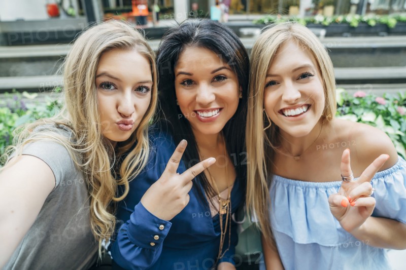 Smiling women posing and gesturing for cell phone selfie