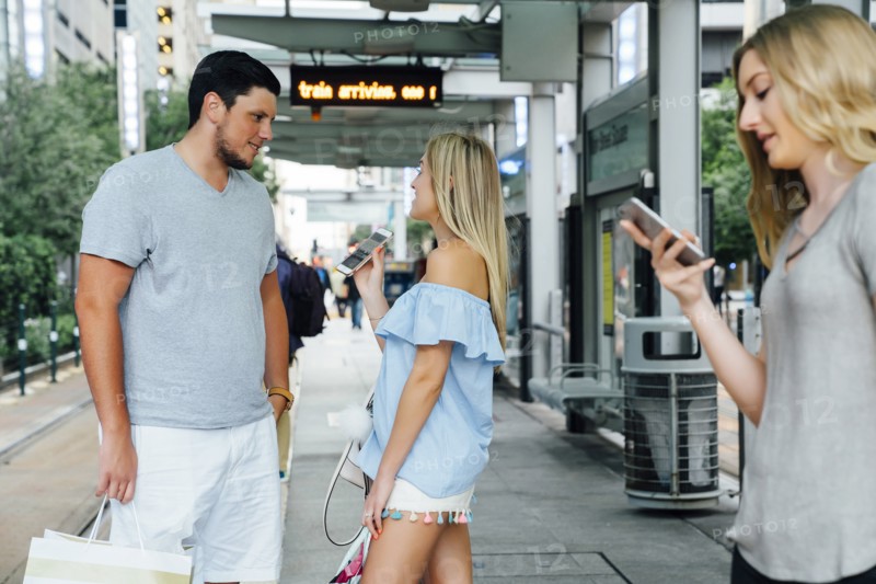 Caucasian woman showing cell phone to man at train station
