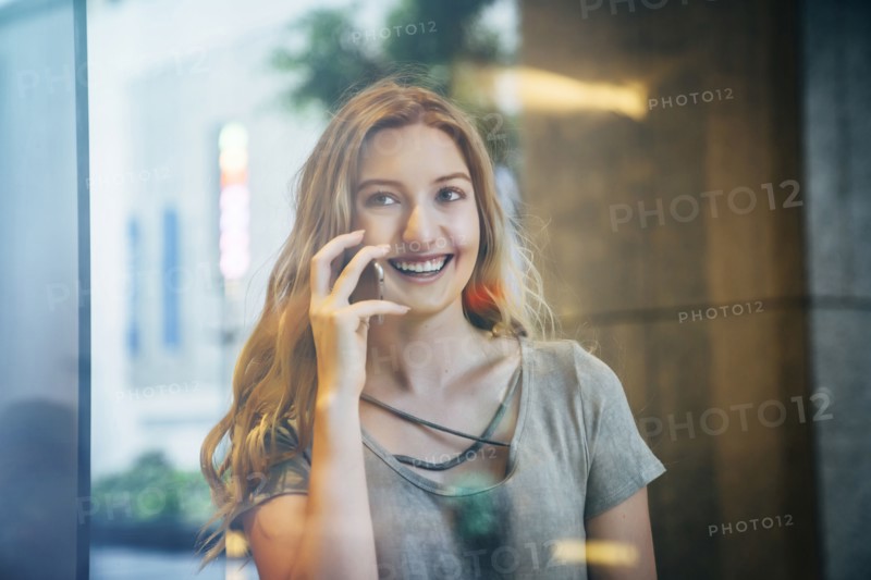 Smiling Caucasian woman talking on cell phone behind window