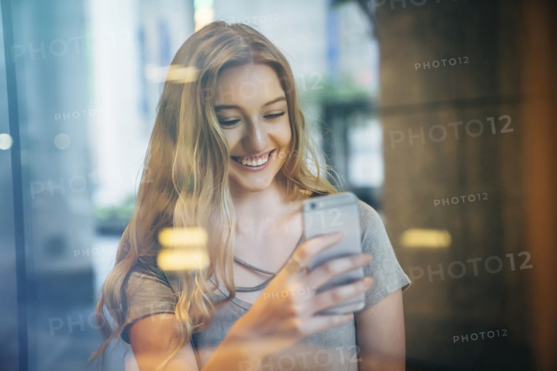 Smiling Caucasian woman posing for cell phone selfie behind window