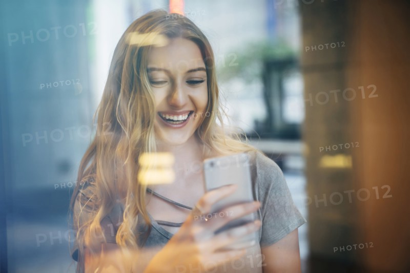 Smiling Caucasian woman posing for cell phone selfie behind window