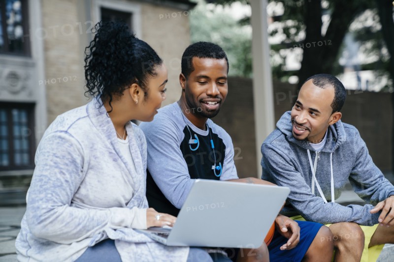Black friends sitting outdoors using laptop