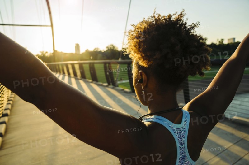 Mixed Race woman wearing earbuds stretching arms on bridge
