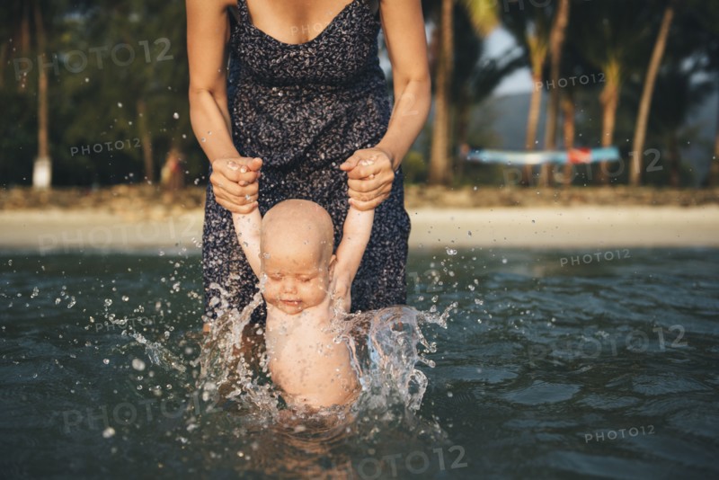 Caucasian mother holding arms of baby daughter splashing in ocean