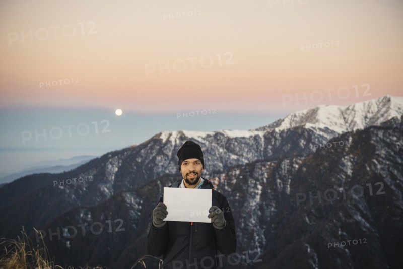 Smiling Caucasian man holding blank sign in mountain landscape