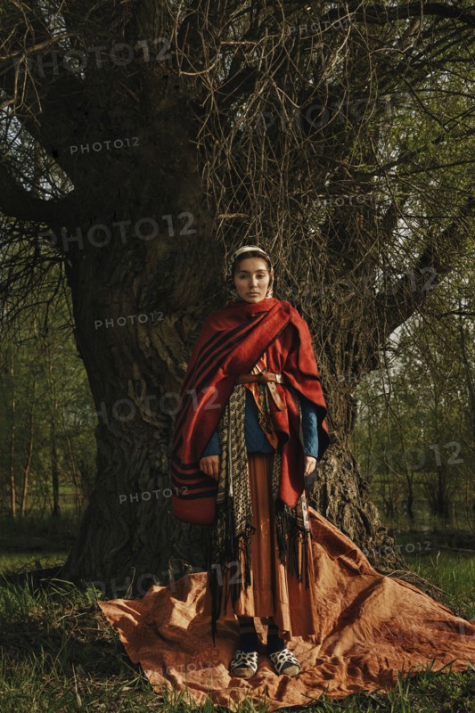 Caucasian woman wearing traditional clothing standing near tree
