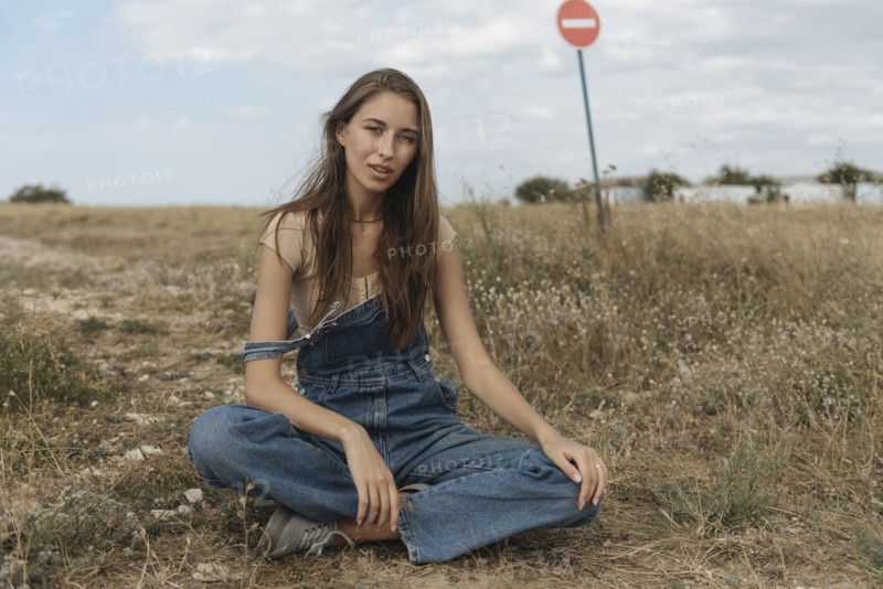 Caucasian woman wearing overalls sitting in rocky field