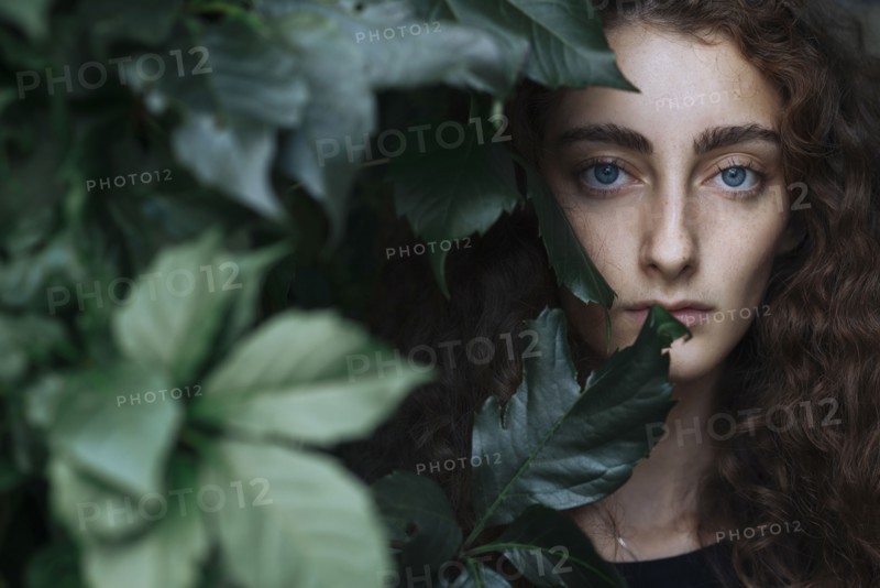 Portrait of serious Caucasian woman behind leaves